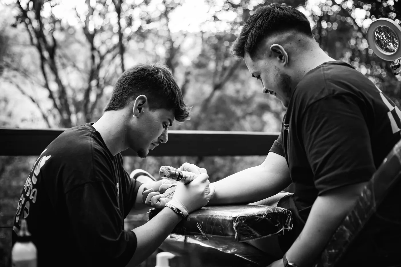 Lipe tatuando ao ar livre, em preto e branco